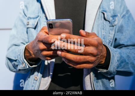 Cropped unrecognizable adult ethnic male in casual wear using mobile phone while standing on the street Stock Photo