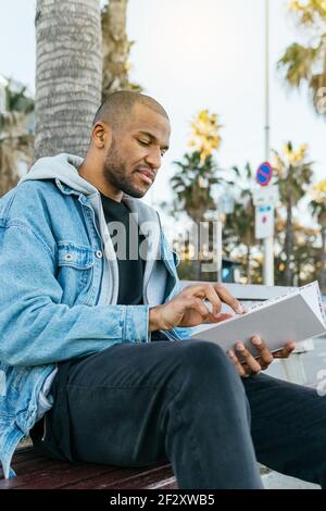 Young tattooed male guitarist playing acoustic guitar while recording video on photo camera in house room Stock Photo