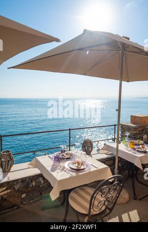 Table set for two in a restaurant facing the Ligurian sea in Camogli, Italy. It's summer season and there is no social distancing at tables Stock Photo