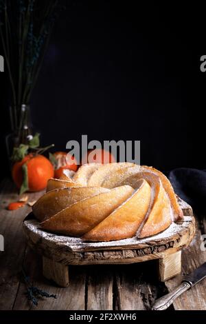 Appetizing sweet homemade bundt cake sprinkled with white sugar powder served on rustic wooden table with fresh tangerines Stock Photo