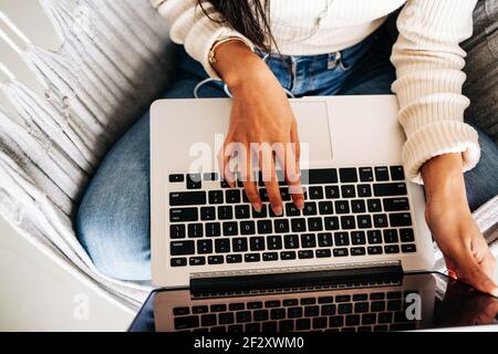 From above of cropped unrecognizable young Woman using touchpad of portable laptop while sitting in hammock indoors Stock Photo