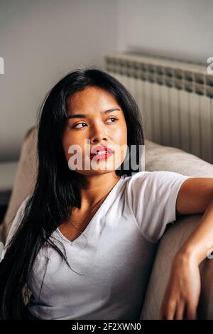 Portrait on serious ethnic female sitting on soft sofa looking away while having free time Stock Photo