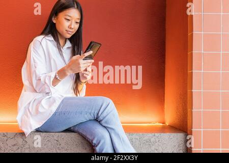 Calm asian Woman in casual clothes sitting in comfortable pose and browsing internet on mobile phone Stock Photo