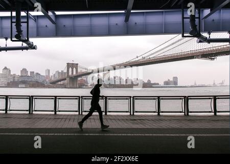 Side view anonymous sportsman jogging on paved embankment against urban city and suspension bridge on gloomy day Stock Photo