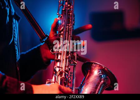 Crop faceless professional musician playing saxophone with fingers on keys during live concert in neon lights Stock Photo