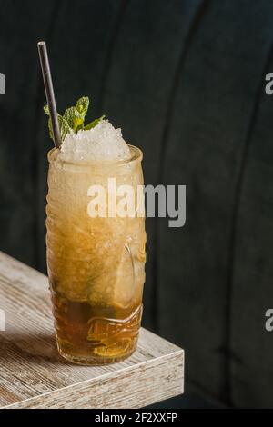 Tiki cup with cold alcohol drink with straw served with ice and decorated with fresh herb placed on blurred background Stock Photo
