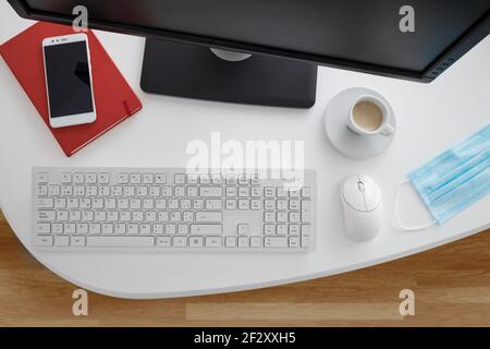 Modern computer and smartphone with notebook placed on white table with medical mask in light office Stock Photo
