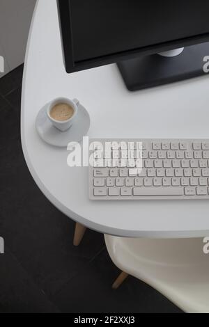 From above modern computer with black monitor and white keyboard placed on desk with coffee mug in office Stock Photo