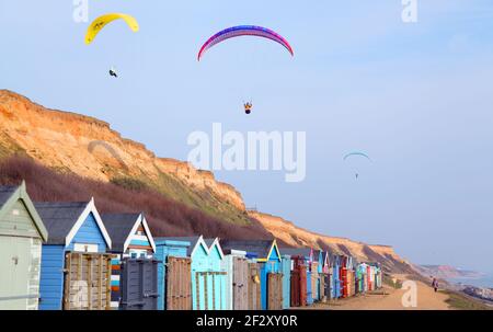 Paragliders paragliding in blue sky above cliffs and beach huts of Barton on Sea, Hampshire Stock Photo