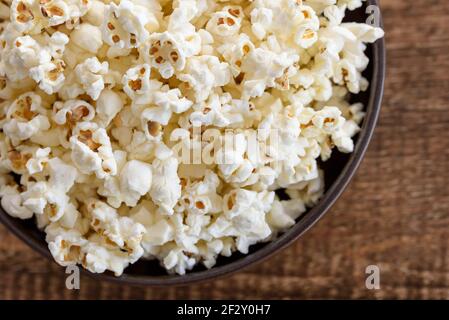 A bowl of popcorn, top-view, warm colors, light brown wooden background, flat lay, daylight macro close-up Stock Photo