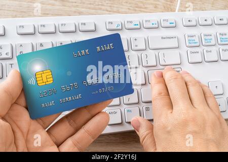 Person hands hold the credit card and press down the enter key on a white computer keyboard. Online shopping and payments, making orders via Internet. Stock Photo