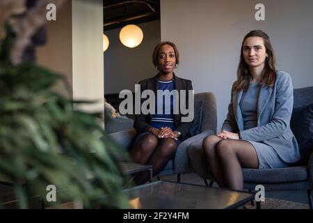 two elegantly dressed business women are sitting on armchairs in the office Stock Photo