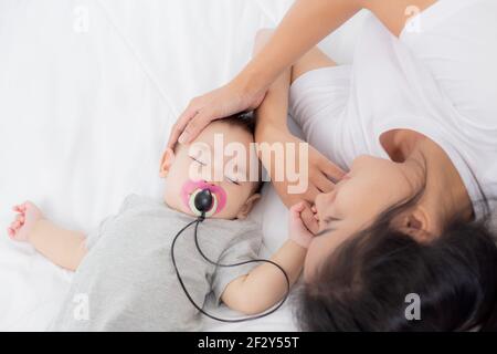 Young asian mother touch head of little baby girl with tender on bed in the bedroom, mom love newborn and care, woman with expression with child toget Stock Photo