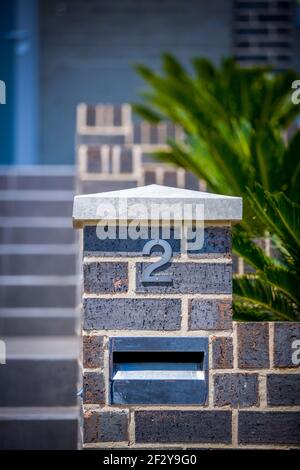 Metallic number 2 on grey brick garden walls contrast with green palms Stock Photo