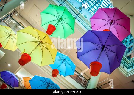 Multiple umbrellas in red pots suspended from ceiling. Red, yellow, orange, blue, pink, purple and green Stock Photo
