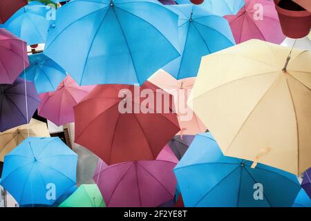 Multiple umbrellas in red pots suspended from ceiling. Red, yellow, orange, blue, pink, purple and green Stock Photo