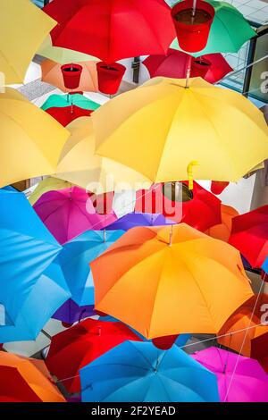 Multiple umbrellas in red pots suspended from ceiling. Red, yellow, orange, blue, pink, purple and green Stock Photo