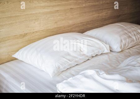 Bedroom with white bed, White two pillows, White duvet on the bed with wooden headboard and sunlight Stock Photo