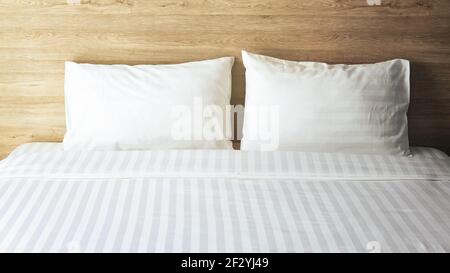 Bedroom with white bed, White two pillows, White duvet on the bed with wooden headboard and sunlight Stock Photo