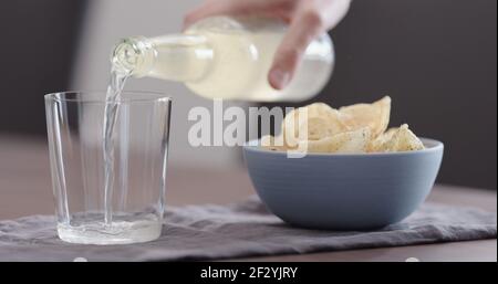man pour ginger beer into tumbler glass with blue bowl full of potato chips, wide photo Stock Photo