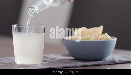 man pour ginger beer into tumbler glass with blue bowl full of potato chips, wide photo Stock Photo