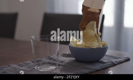 potato chips with ground pepper and salt poured into blue bowl with tumbler glass on wood table, wide photo Stock Photo
