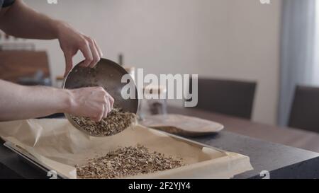 man making granola pour it on baking tray with parchment paper, wide photo Stock Photo