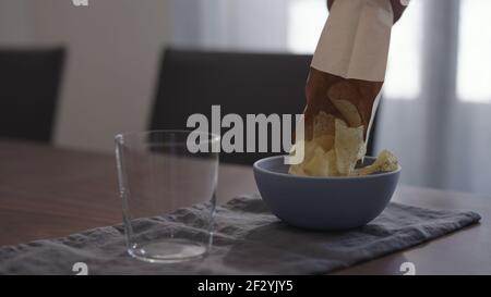 potato chips with ground pepper and salt poured into blue bowl with tumbler glass on wood table, wide photo Stock Photo