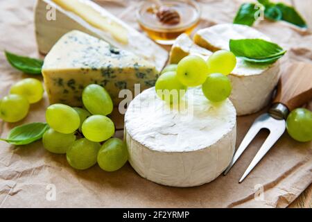 Various types of cheese, basil and grapes on a table Stock Photo