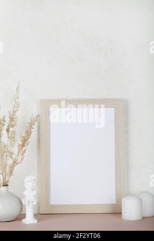 Portrait empty wooden frame mockup, dried pampas grass, small statue and candles on white background, interior, home design. Art concept. copy space.  Stock Photo