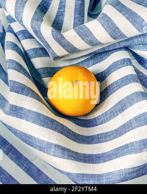 The concept of mindful consumption. Minimalistic summer composition with fresh, ripe orange on a striped, textile background. Healthy season fruits wi Stock Photo