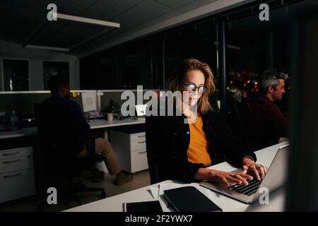 Portrait of a young businesswoman busy working on laptop in office with colleagues at background Stock Photo