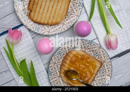 Pink Colored Easter egg in plate on a breakfast table with jam and pink white tulips and toasted bread. Stock Photo