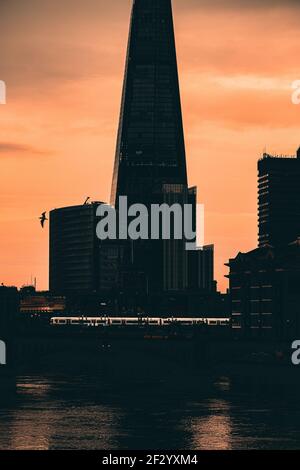 London UK February 2021 Dark late sunset over the city of London, orange sky showing silhouettes of Londons tall skyscrapers. Bright white tube train Stock Photo
