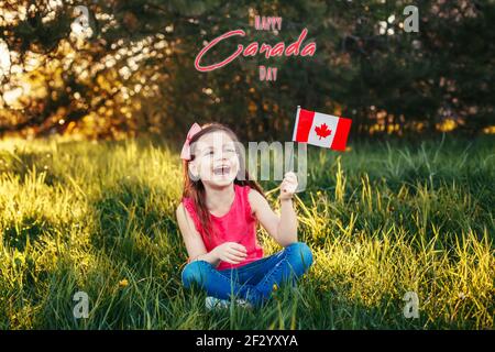 Happy Canada Day. Greeting card with text. Caucasian smiling laughing girl holding Canadian flag. Happy child waving Canada flag in park. Kid citizen Stock Photo
