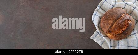 Loaf of rye artisan bread on a kitchen towel on a dark background. Layout with copy space. Stock Photo