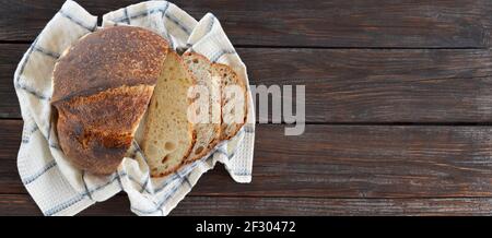 Sliced artisan bread with a crisp crust on a kitchen towel on a old wooden table with copy space. Stock Photo