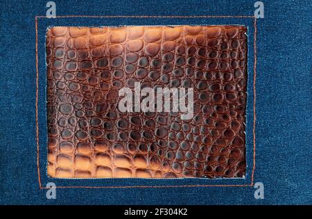 Frame made of blue denim, decorated with orange stitching. Denim lying on crocodile skin. Top view Stock Photo