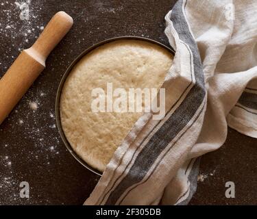 Raw yeast dough resting and rising in large metal bowl covering with linen towel  Stock Photo