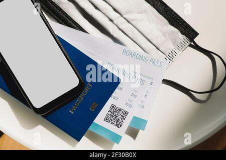 Post covid 19 travel concept. Generic phone with blank screen, a passport, airline boarding pass and a face mask on a table Stock Photo