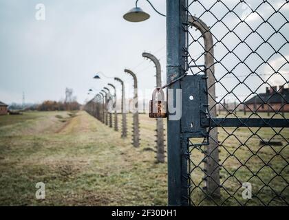 Padlock and chain on gate of world war 2 concentration prisoner of war camp locked with high voltage electric barb wire fence and old retro guard spot Stock Photo