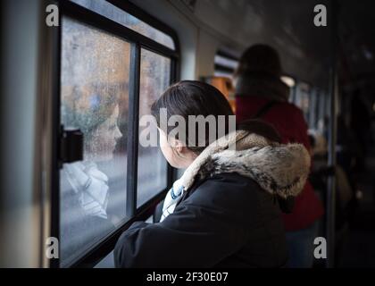 Woman standing on train looking out of window with face reflection mirror on tram glass of tourist passenger reflected on bright sunny day Stock Photo