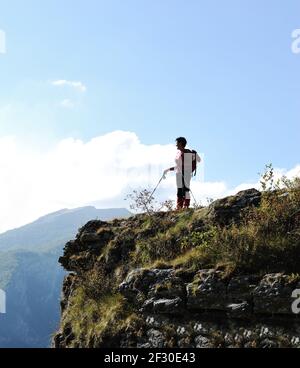 Woman with backpack standing on cliff's edge and looking to a sky with clouds Stock Photo