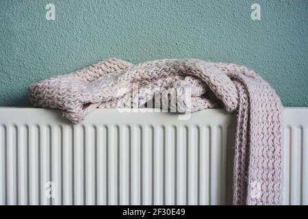 Soft knitted pink scarf drying on a heating radiator after getting wet. Stock Photo