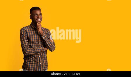 Portraif Of Pensive Dreamy African American Guy Standing Isolated On Yellow Background Stock Photo