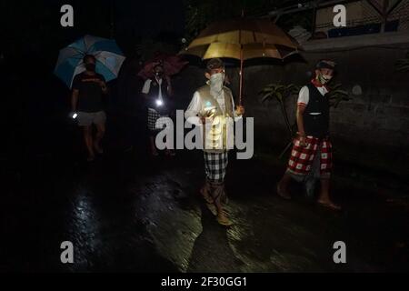 Denpasar, Bali, Indonesia. 14th Mar, 2021. Municipal workers and Sumerta Kelod village-volunteers walks in the rain as they heading back from helping a mother who is about to give birth amid night of Nyepi. Nyepi is the Balinese Hindu holiday of self-reflection in which all activities are stopped and people are not allowed to get outside with all the lights kept low, no working and no pleasures. (Credit Image: © Dicky BisinglasiZUMA Wire) Credit: ZUMA Press, Inc./Alamy Live News Stock Photo