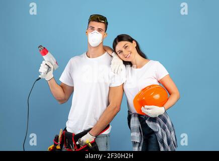 Young couple ready for repair, posing with construction tools over blue background Stock Photo