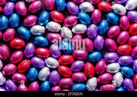 A portrait of a lot of colorful chocolate easter eggs wrapped in colored tin foil. There are red, blue, white, purple and pink eggs all with their own Stock Photo