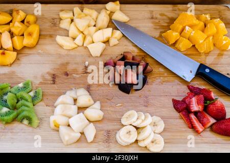 Chopped fruits arranged on cutting board on white wooden background, top view. Ingredients for fruit salad. From above, flat, overhead. Stock Photo