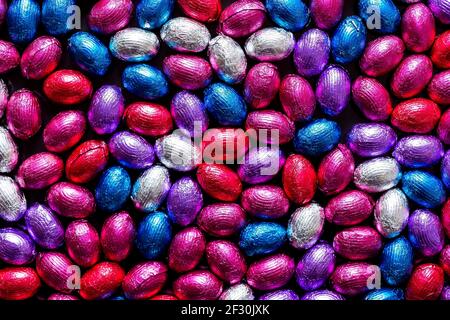 A portrait of a lot of colorful chocolate easter eggs wrapped in colored tin foil. There are red, blue, white, purple and pink eggs all with their own Stock Photo